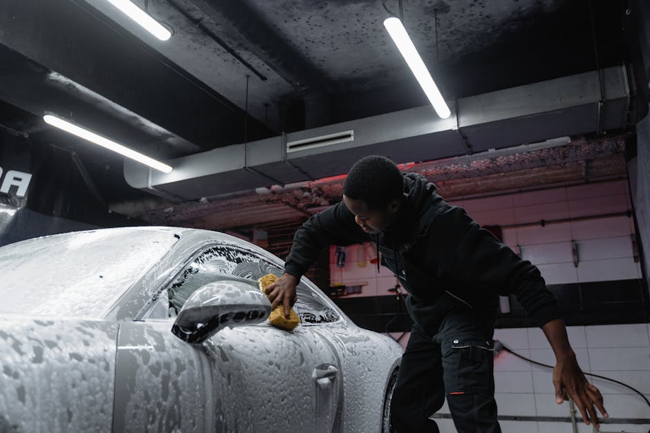 Man cleaning a car with soap and sponge at an indoor carwash facility.