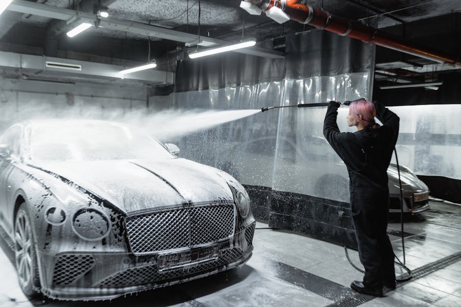 A woman expertly cleans a car using snow foam in a modern indoor car wash facility.